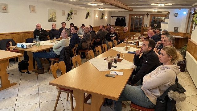 Foto Publikum an Tischen lauscht Präsentation